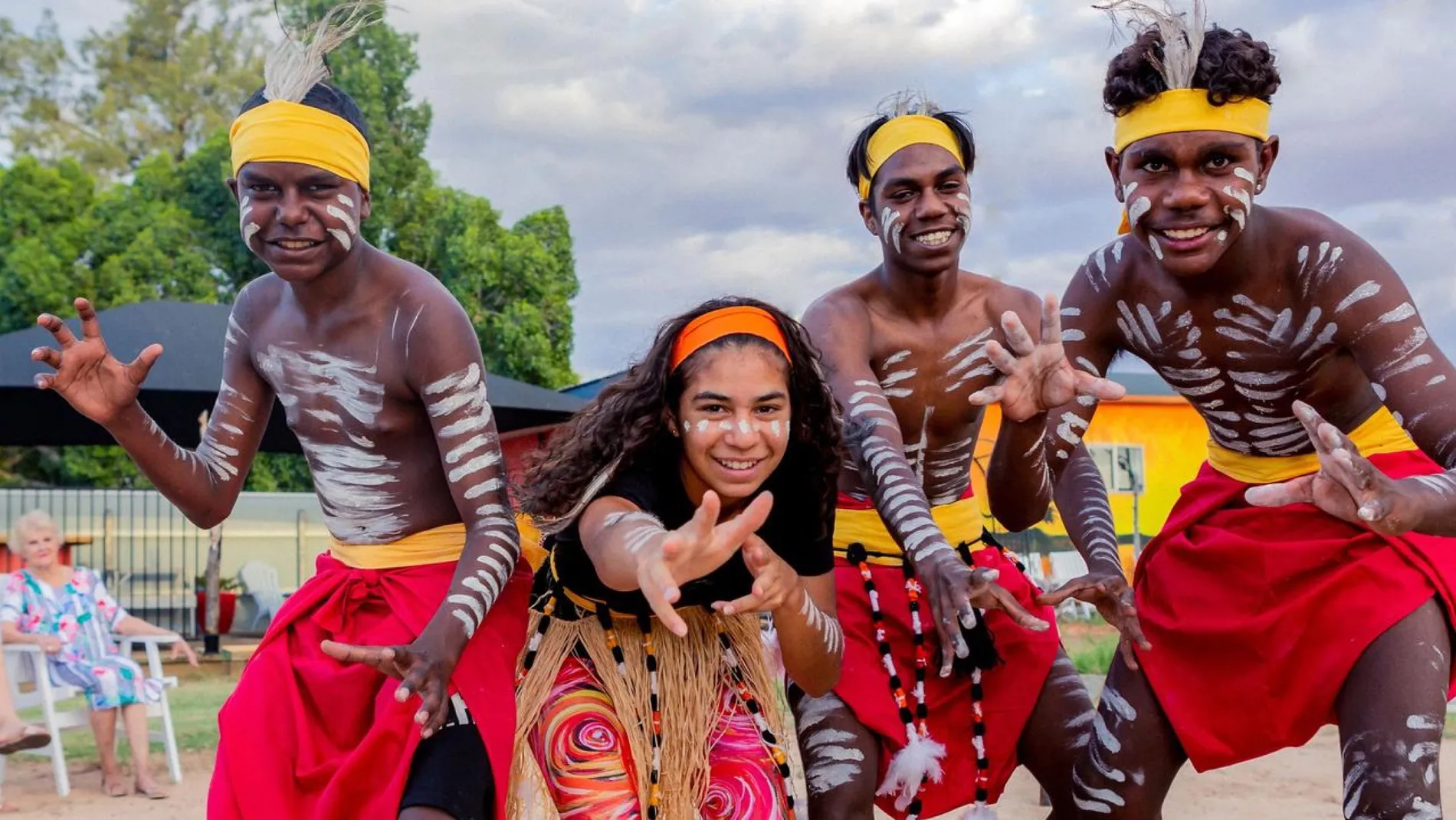 Four Desert Dust Dancers in ochre body paint and red and yellow costume, posed at the Desert Dreaming Centre.