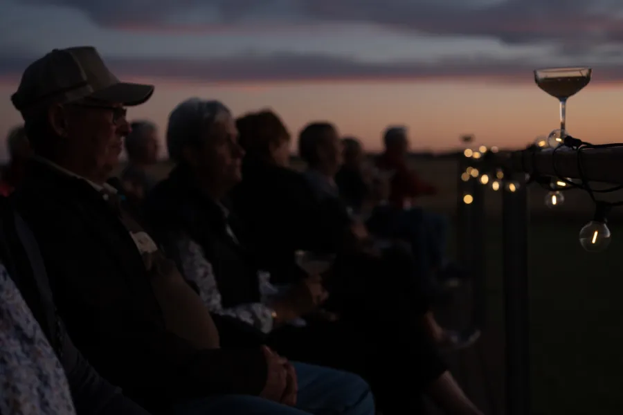 Guests seated with drinks on a deck, watching the sun set over the plains.