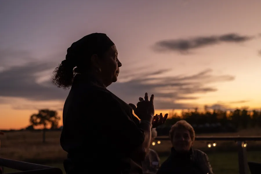 A guide speaks to seated guests, silhouetted against an orange and purple sunset.