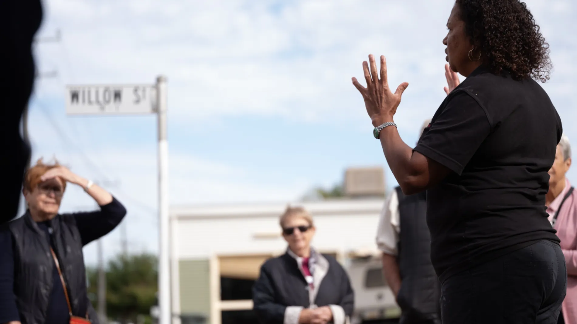 A guide gestures while speaking to a group of visitors on a Barcaldine street under a wide sky.